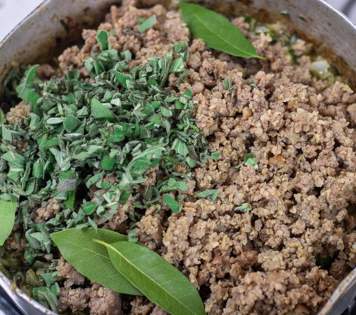 sausage, bay leaves and sage added to onions in a frying pan for oyster dressing