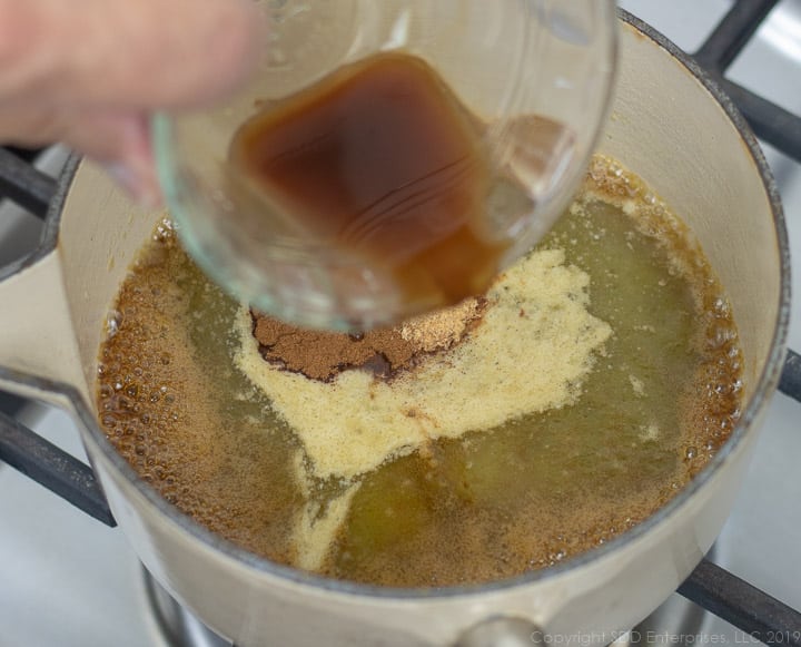 spices and vanilla extract being added to the butter and cane syrup in a sauce pan for cane syrup rum sauce