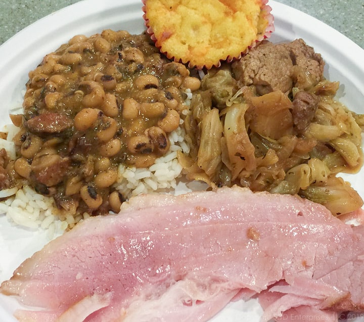black-eyed peas over rice with baked ham and smothered cabbage on a white paper plate