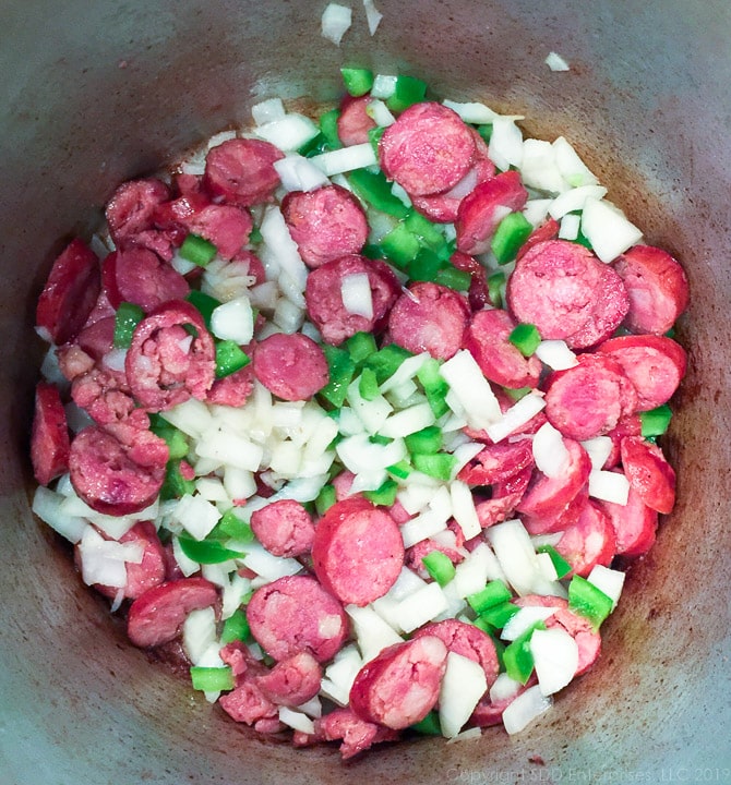 andouille sasage, yellow onions and bell peppers frying in a stockpot for b;ack-eyed peas