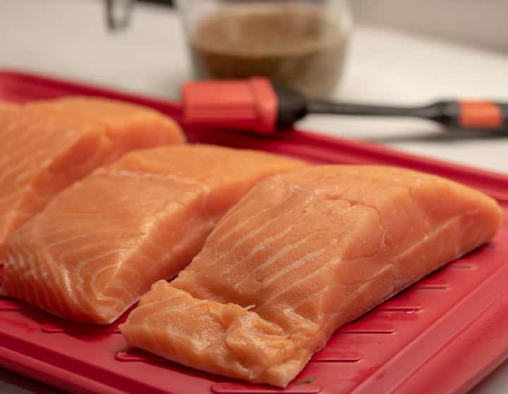 fresh uncooked salmon filets on a red platter with a brush and marinade