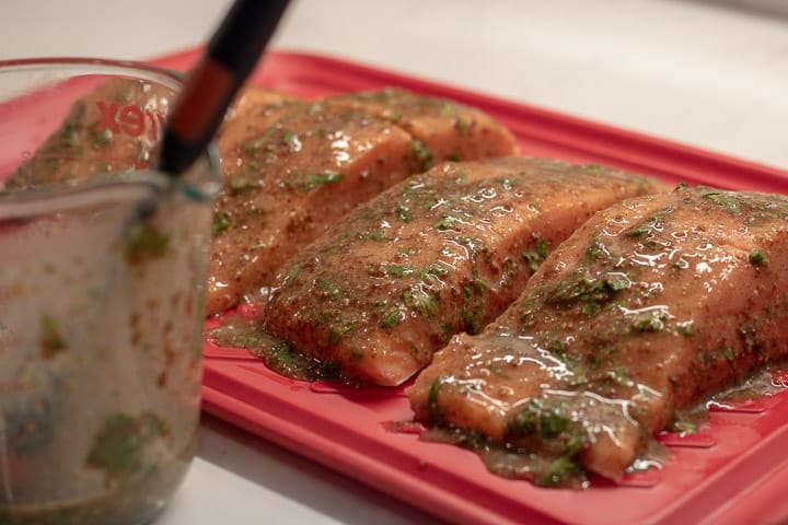 salmon marinating with cilantro creole mustard marinade on a red platter with extra marinade in a measuring cup