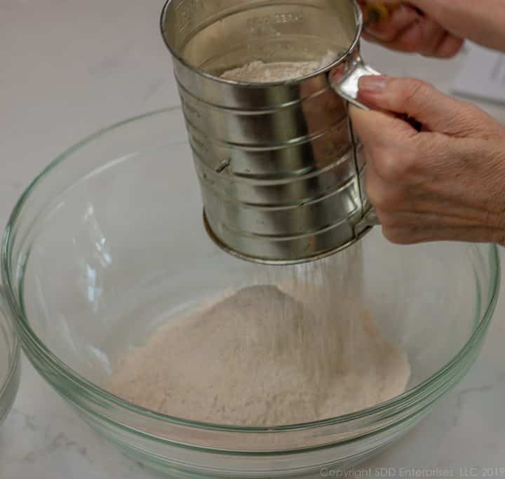 sifting flour and spices into a glass bowl for fruitcake