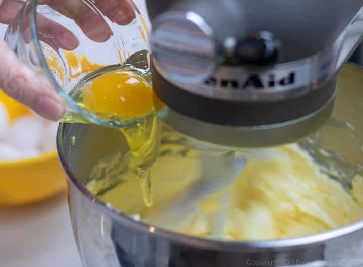 eggs being added to batter in a mixing bowl for fruitcake