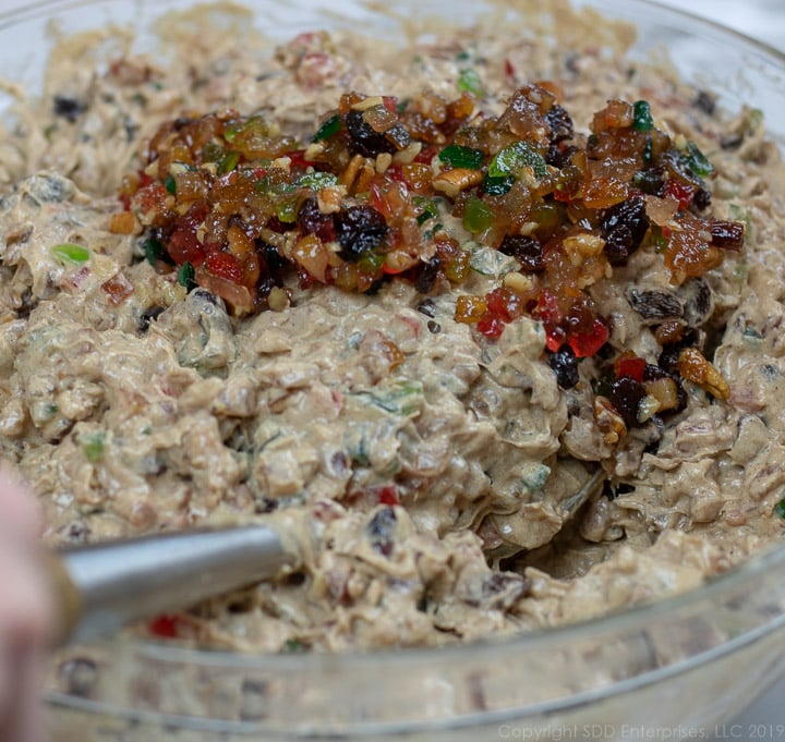 Mixed fruit being added to batter in a bowl for fruitcake.