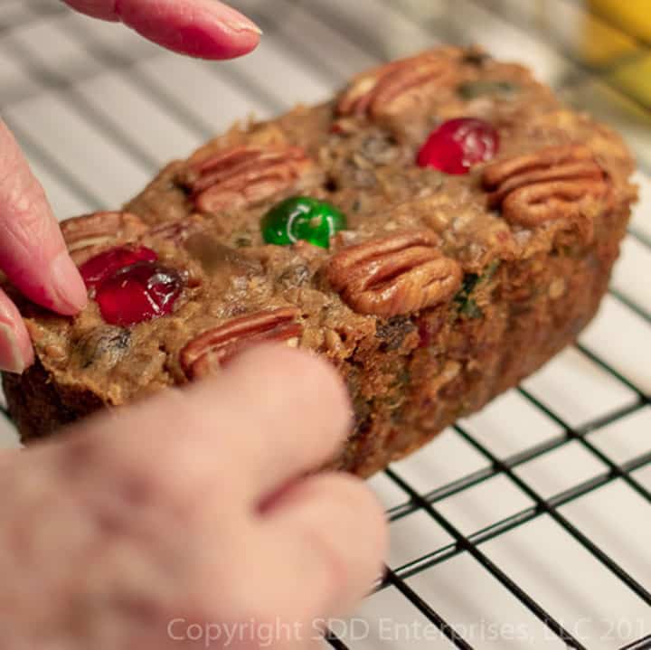 Two hands on a fruitcake on a cooling rack.