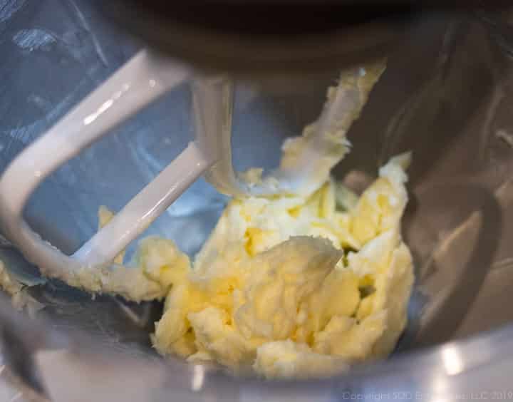 butter being creamed in a mixing bowl by a stand mixer for fruitcake cookies