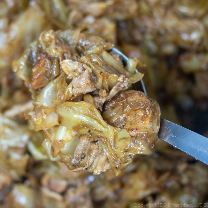 smothered cabbage with pork in a spoon over a pot of smothered cabbage