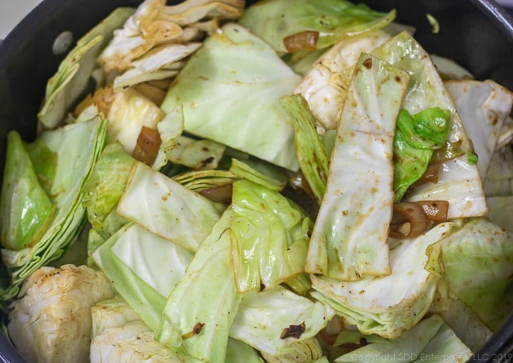 chopped cabbage being added to onions in a dutch oven for smothered cabbage