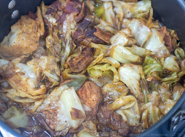 cabbage and pork simmering in a dutch oven for smothered cabbage