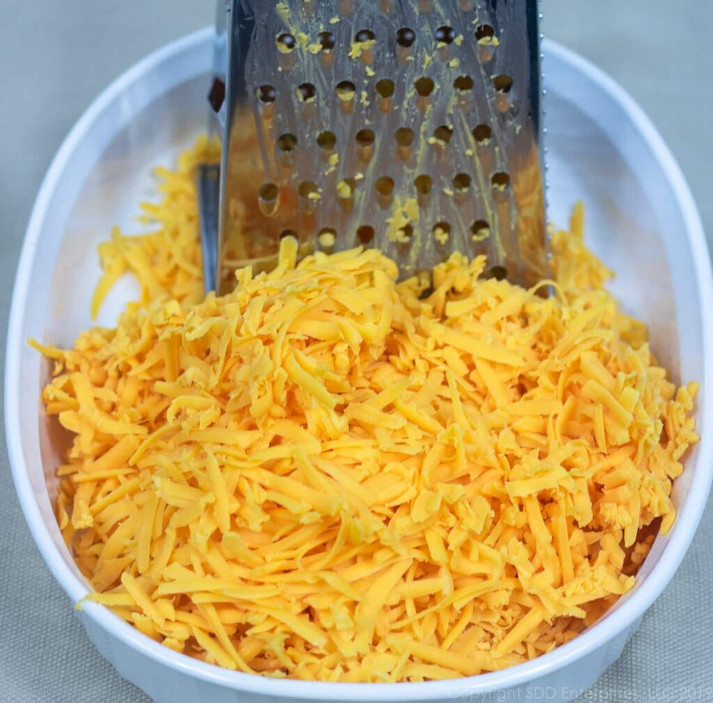 grated sharp cheddar cheese in a bowl with a grater for macaroni and cheese