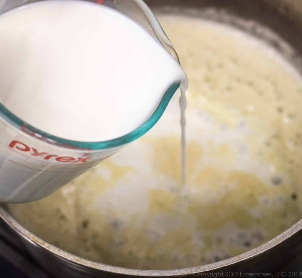 adding warm milk to the blond roux for macaroni and cheese
