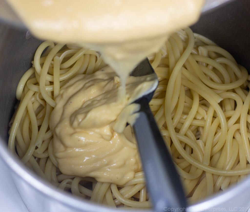 adding the cheese sauce to the cooked noodles for macaroni and cheese