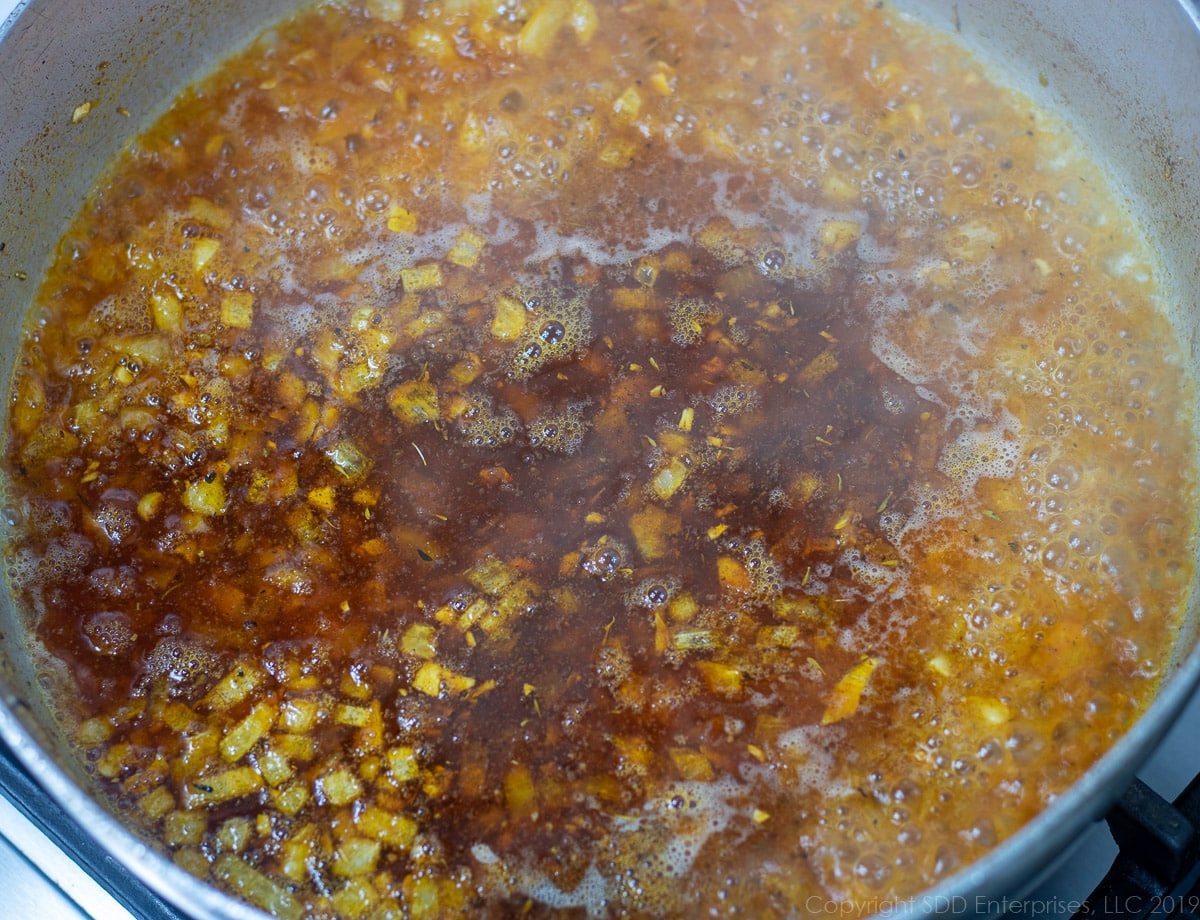 creole seasoning and wine added to sauteed onions in a frying pan