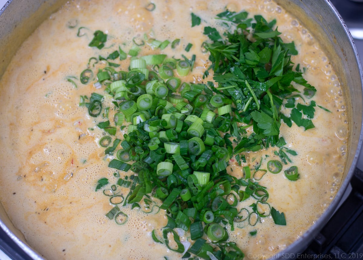 chopped green onions and parsley added to crawfish and cream in a frying pan