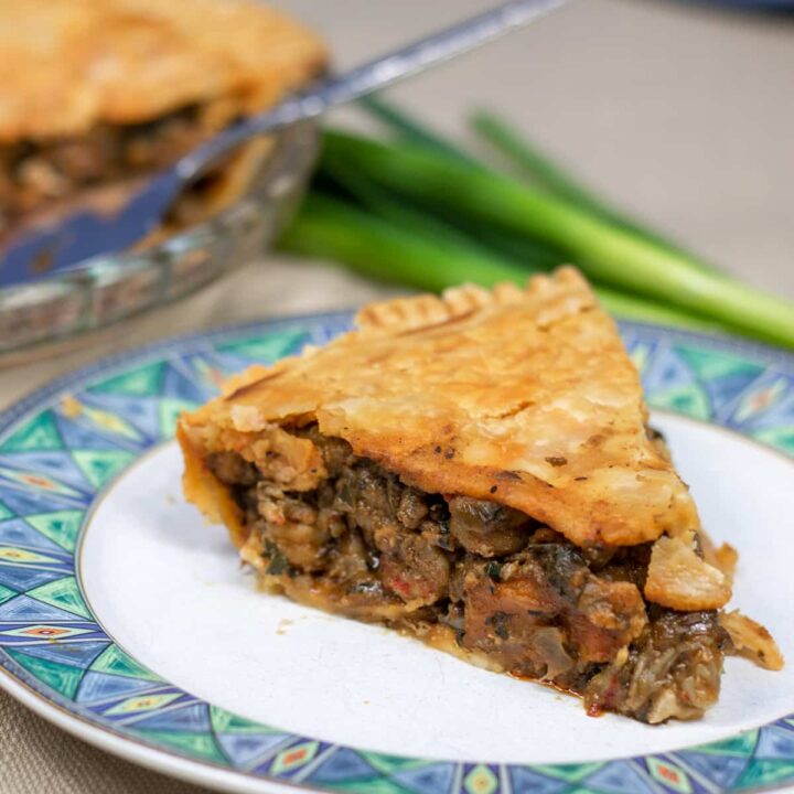 slice of crawfish pie on a plate with crawfish pie and green onion in background