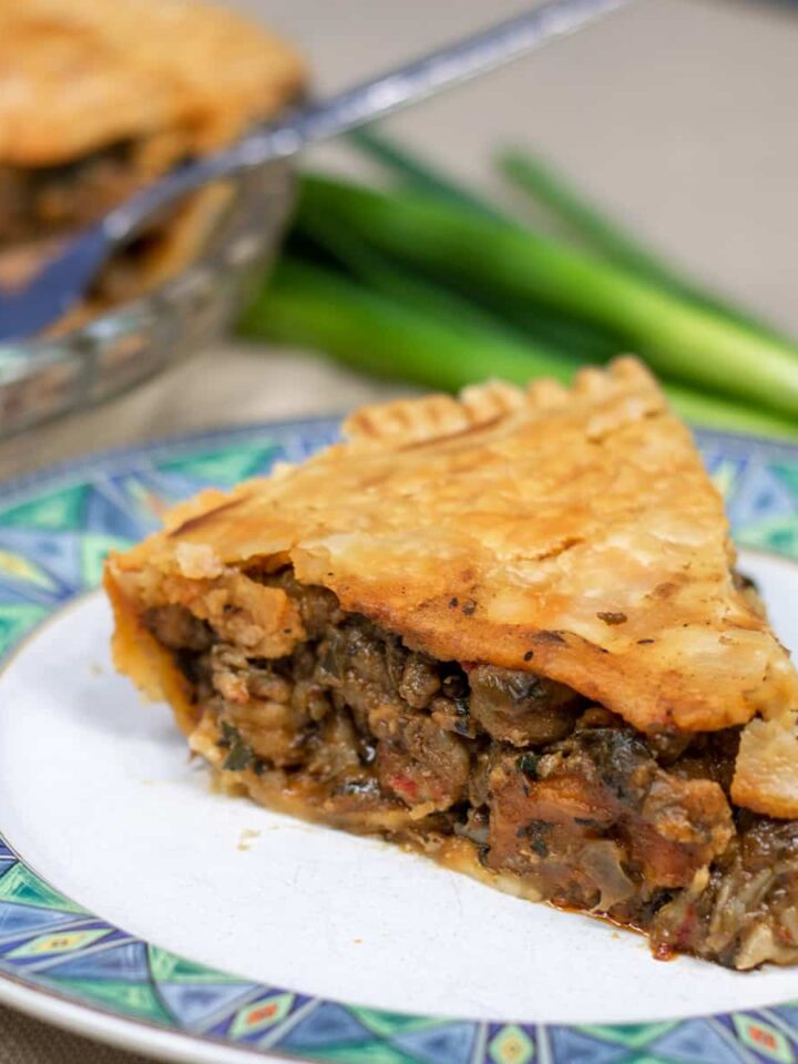 slice of crawfish pie on a plate with crawfish pie and green onion in background