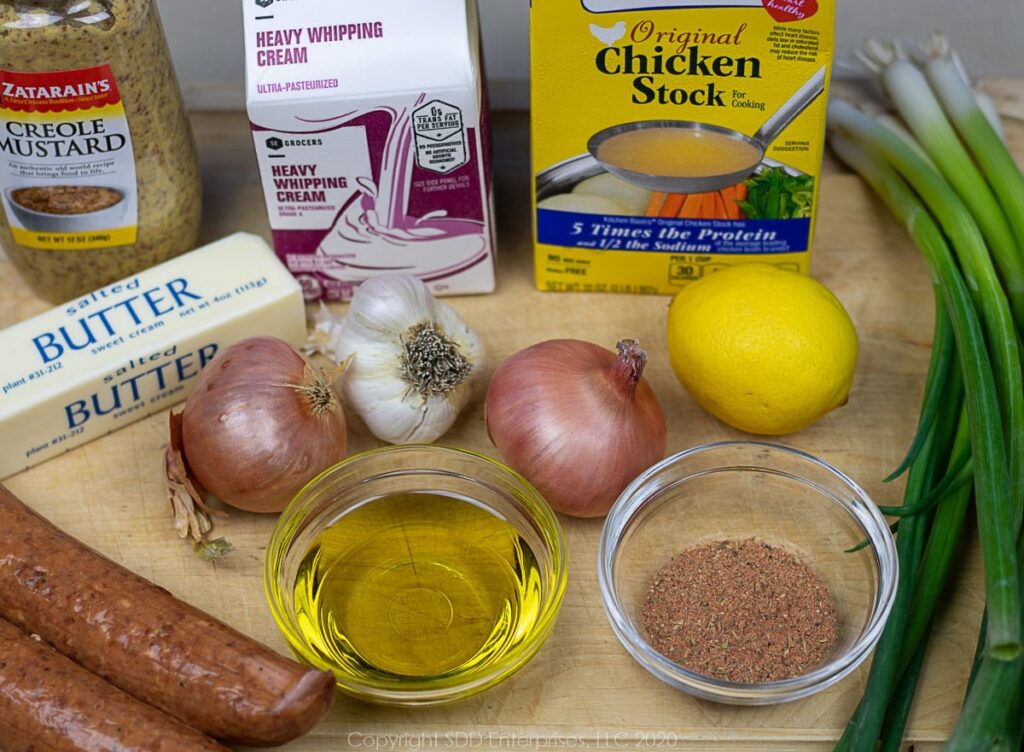 shallots, garlic, green onions, lemon, sausage, cream. stock, creole mustard and creole sesoning on a cutting board
