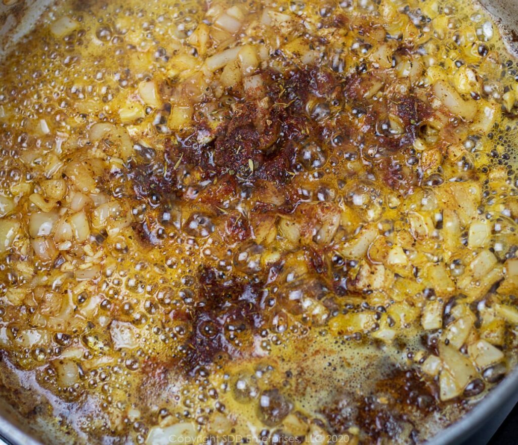 garlic and creole seaoning added to shallots in a frying pan