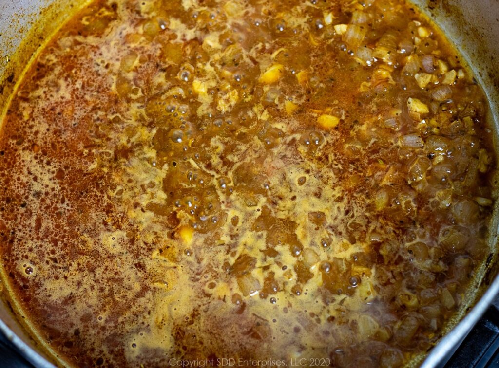 stock added to a frying pan with spices and seasoning