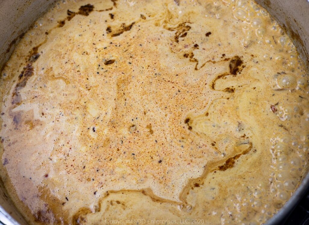 heavy cream added to stock and spices in a frying pan