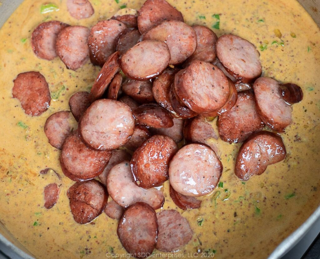 fried sausage added to sauce in a frying pan