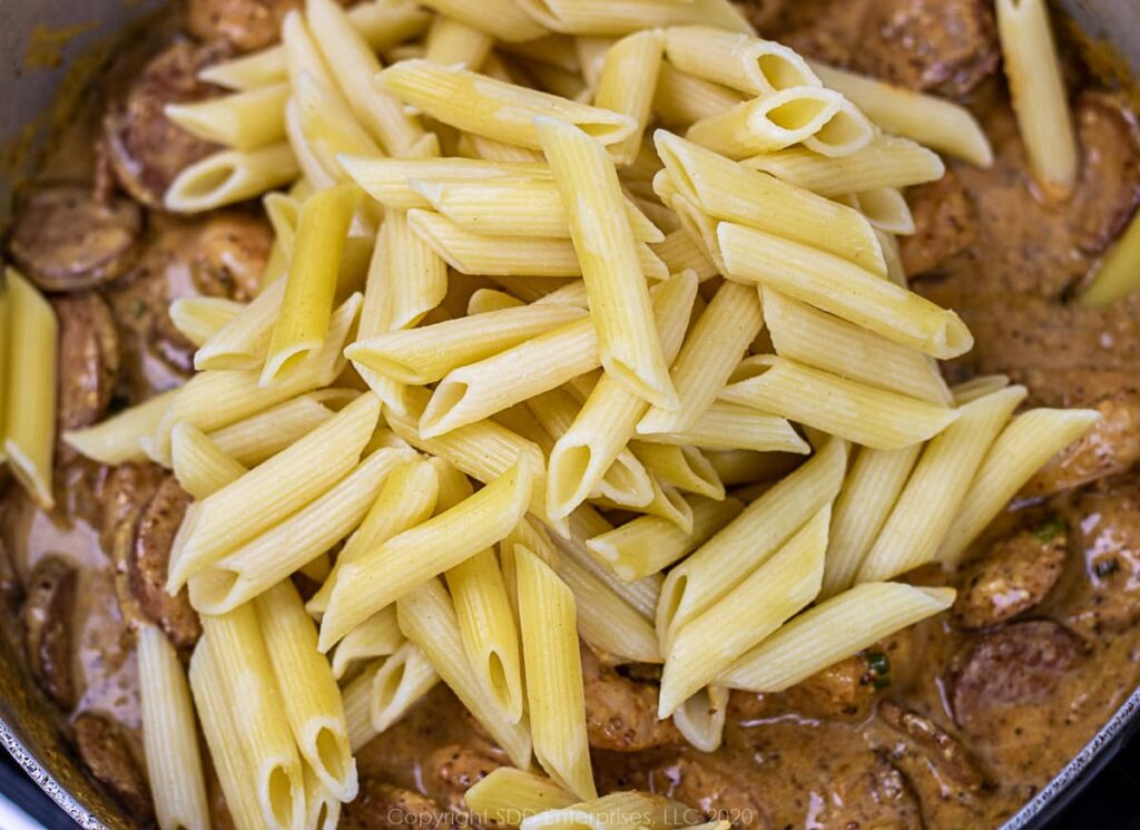 cooked pasta being added to the sauce in a frying pan