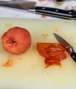 a peeled tomato with skin and knife on a cutting board