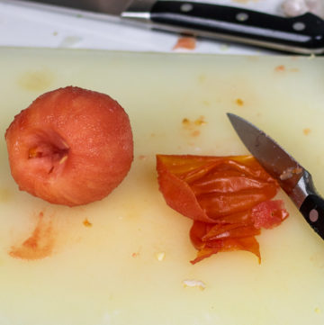 a peeled tomato with skin and knife on a cutting board