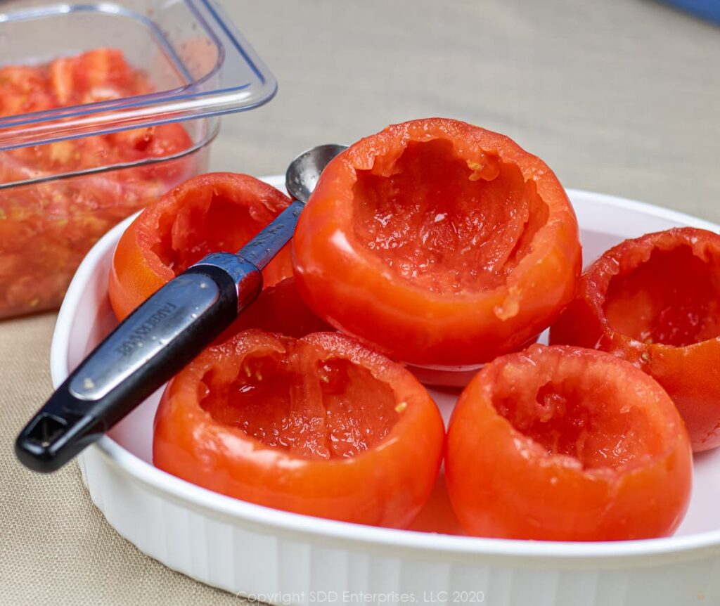 hollowed out tomatoes with a melon baller in a pyrex dish