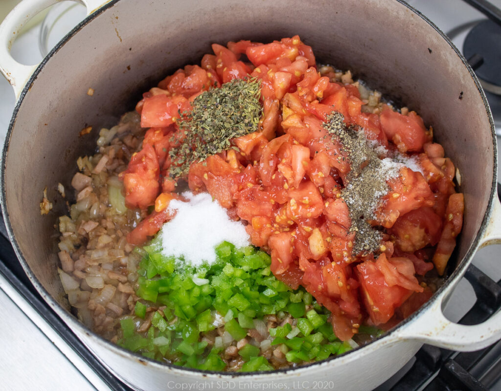 chopped tomaties, peppers, garlic and herbs added to onions and ham in a dutch oven