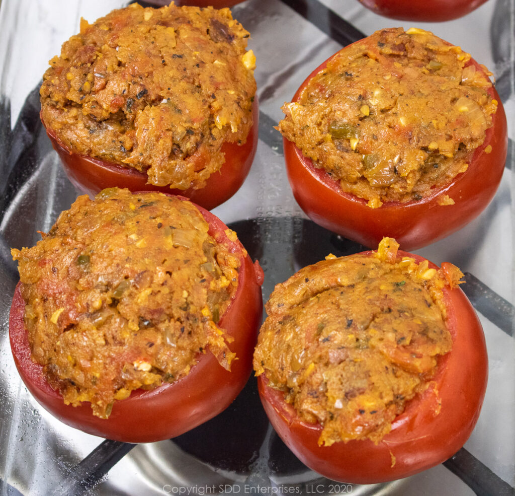 four uncooked tomatoes stuffed with filling in a baking dish