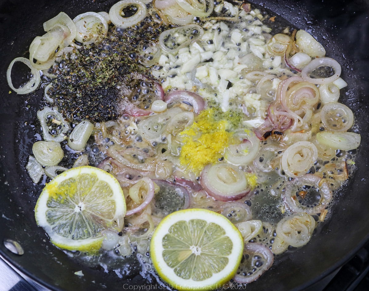 herbs and spices, lemon zest, garlic and lemon peels added to sauteing shallots in a skillet