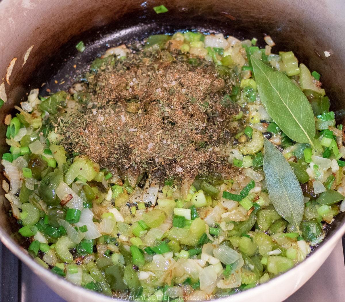 onions, bell peppers and celery cooking in a dutch oven with spices and bay leaves