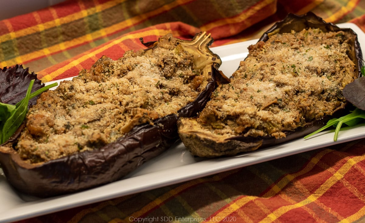 two roasted shrimp stuffed eggplant on a white platter and a cloth background