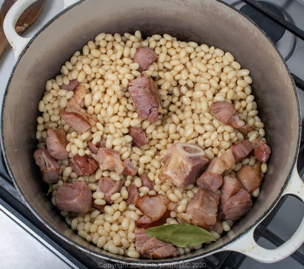 dry navy beans and bay leaves added to fried ham and bacon in a Dutch oven