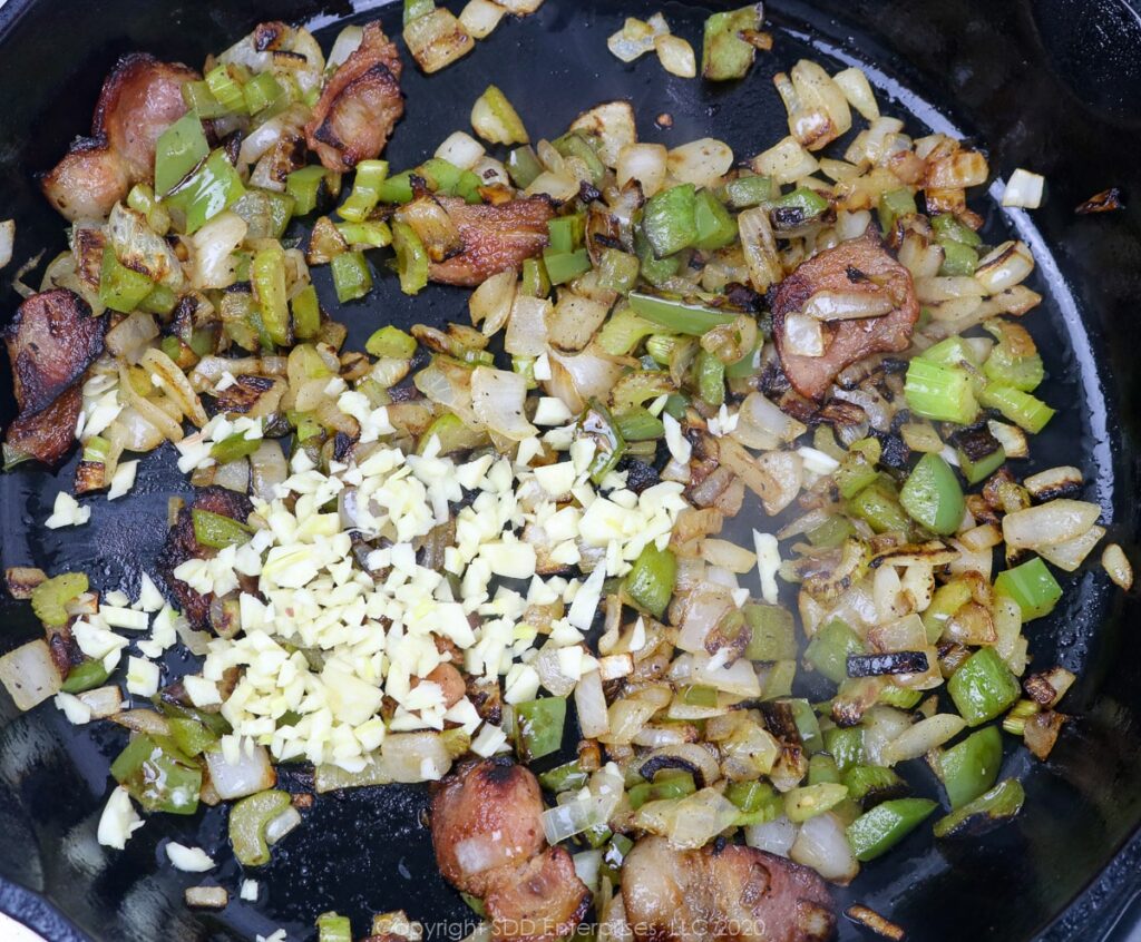 yellow onions, bell peppers, celery and garlic sauteeing in bacon fat in a cast iron skillet