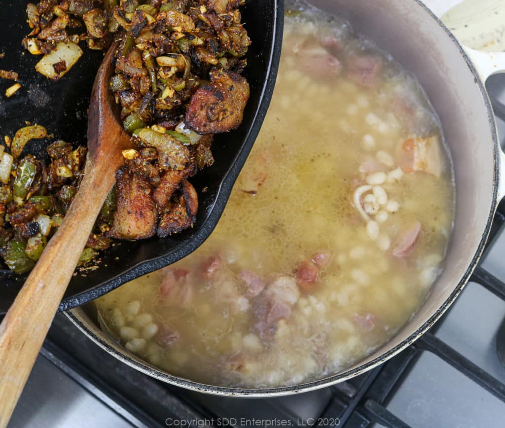 adding sauteed vegetables into simmering navy beans in a dutch oven