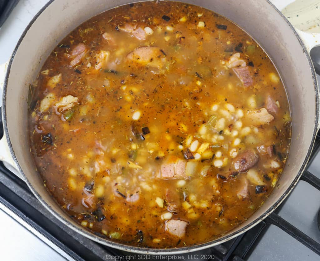 simmering navy beans with vegetables and meats in a dutch oven