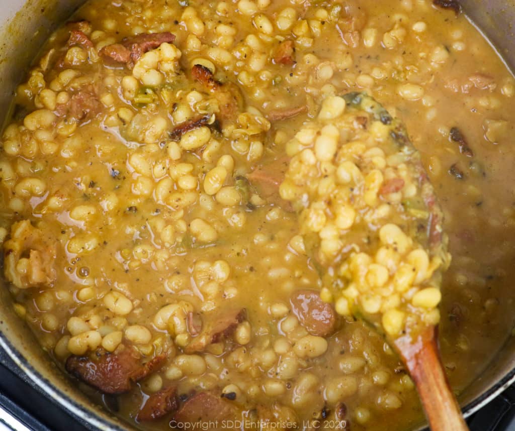 navy beans and ham simmering in a dutch oven with a wooden spoon