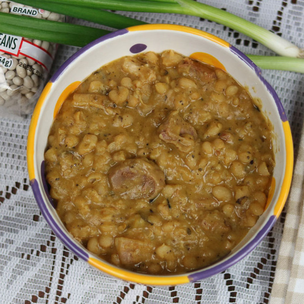 white beans and ham in a yellow, purple nd white bowl with green onion garnish and dry navy beans