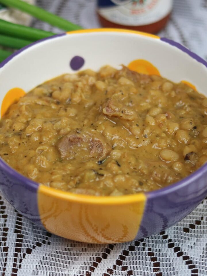 white beans and ham in a purple and yellow and white bowl with green onion garnish