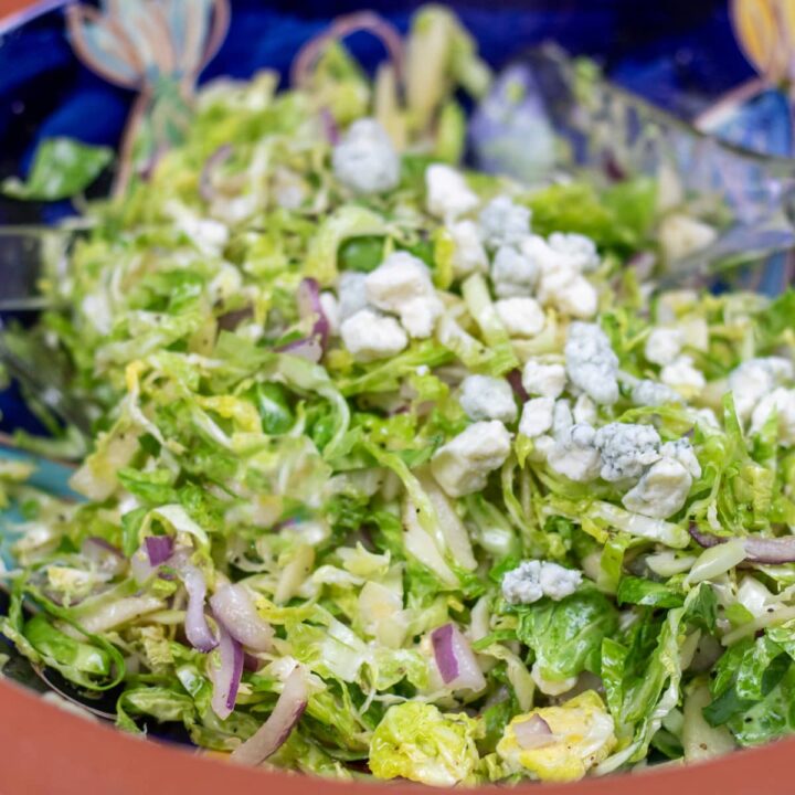 brussels sprouts coleslaw with blue cheese in a blue and brown bowl with salad tings