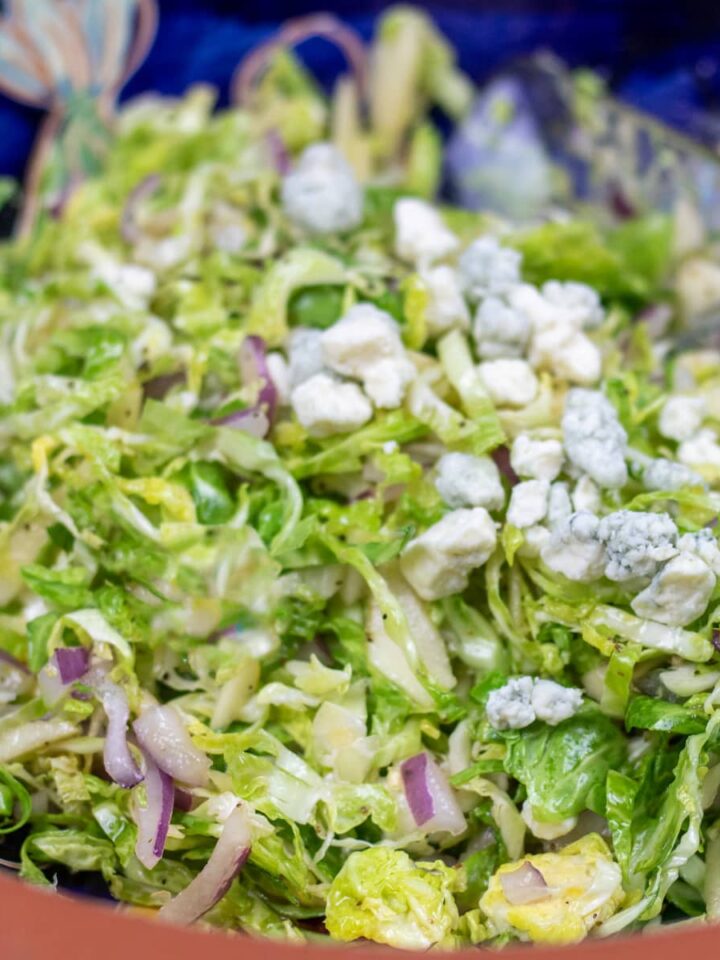 brussels sprouts coleslaw with blue cheese in a blue and brown bowl with salad tings