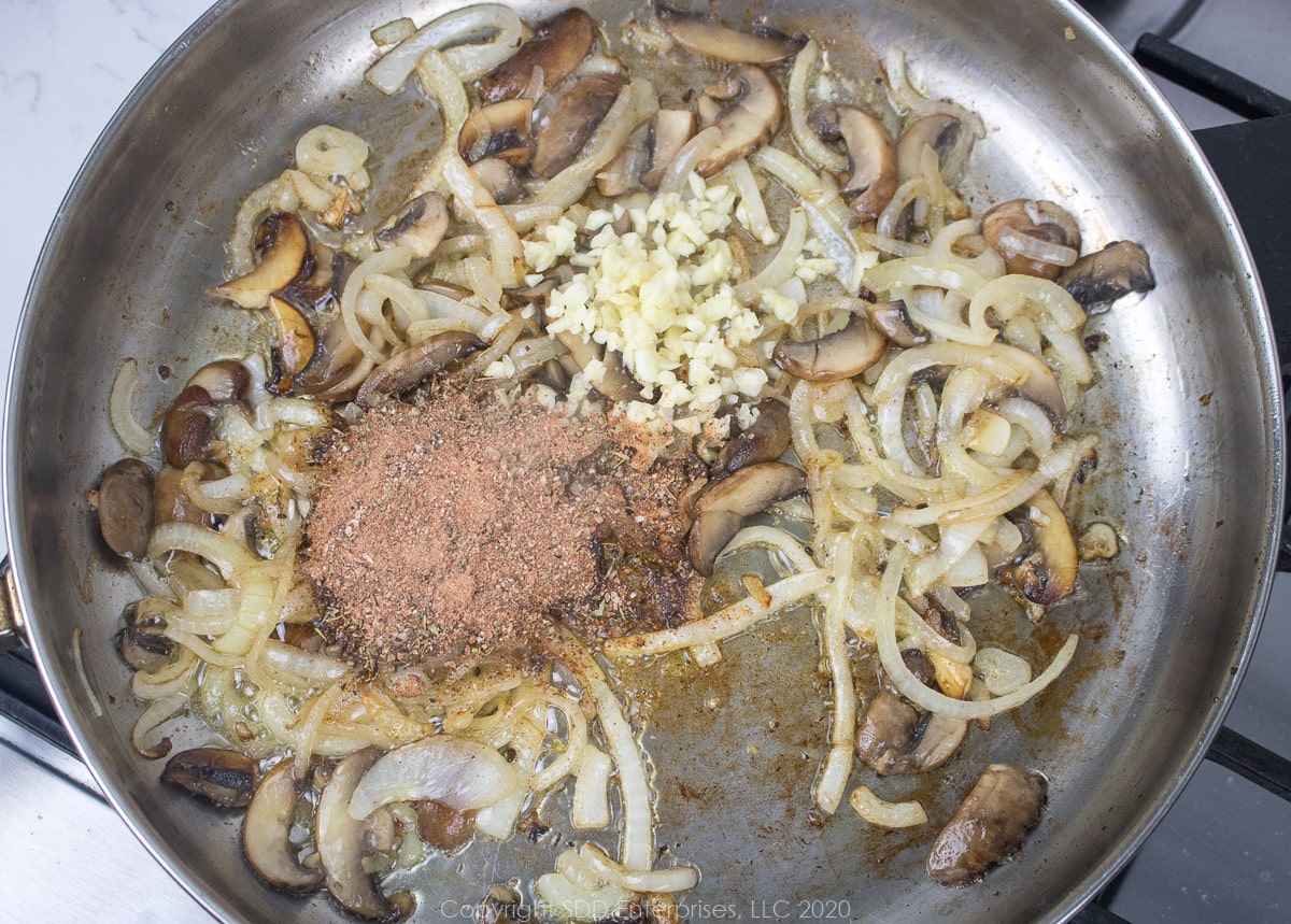 garlic and spices added to mushrooms and onions in a frying pan