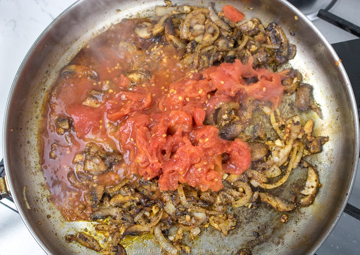 crushed tomatoes added to onions, mushrooms and spices in a frying pan