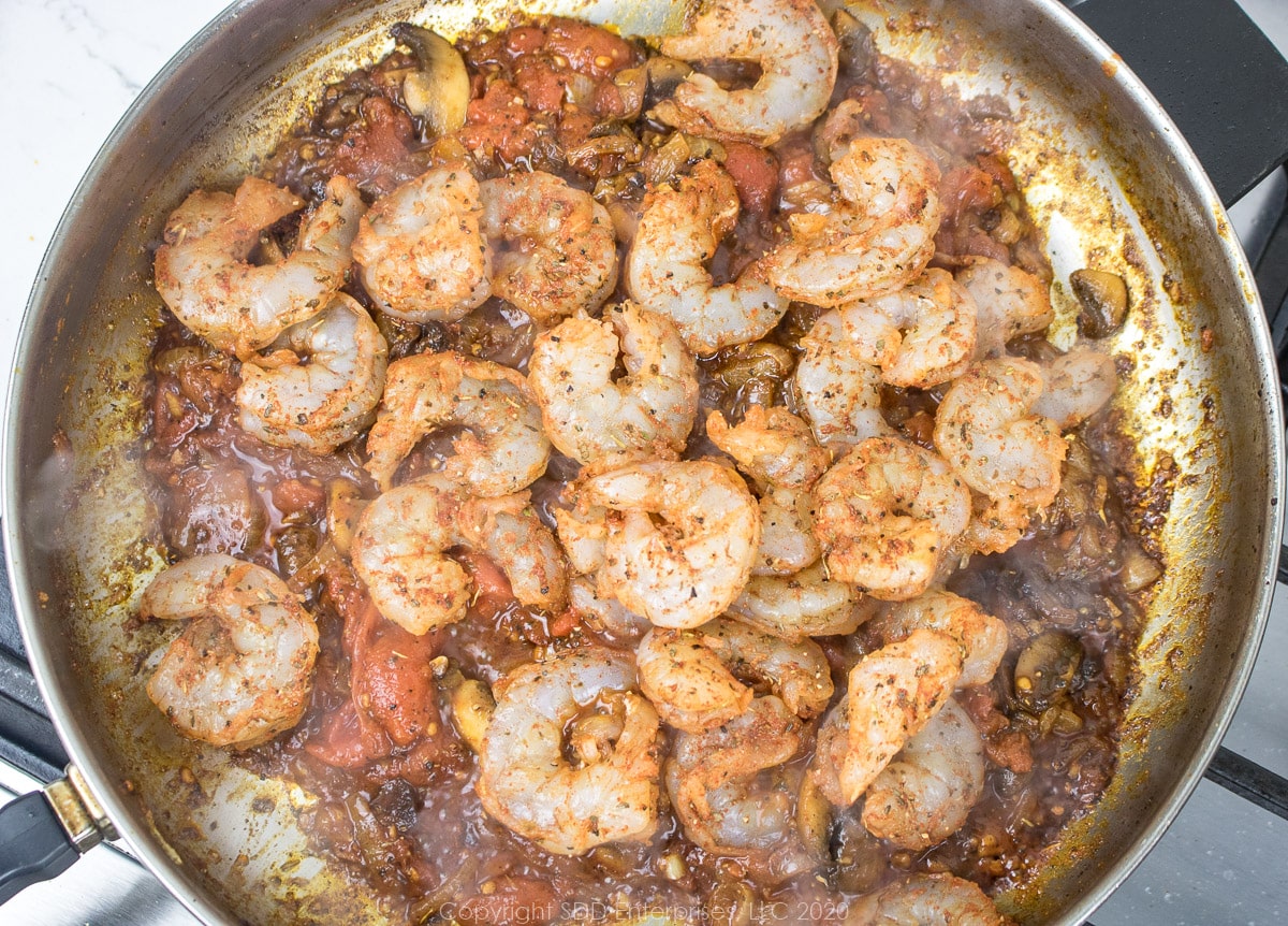 seasoned shrimp added to the mushroom, onions, tomatoes and spices in a frying pan