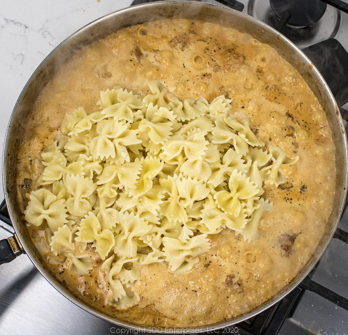 cooked bow tie pasta added to the cream sauce in a frying pan for creamy shrimp pasta