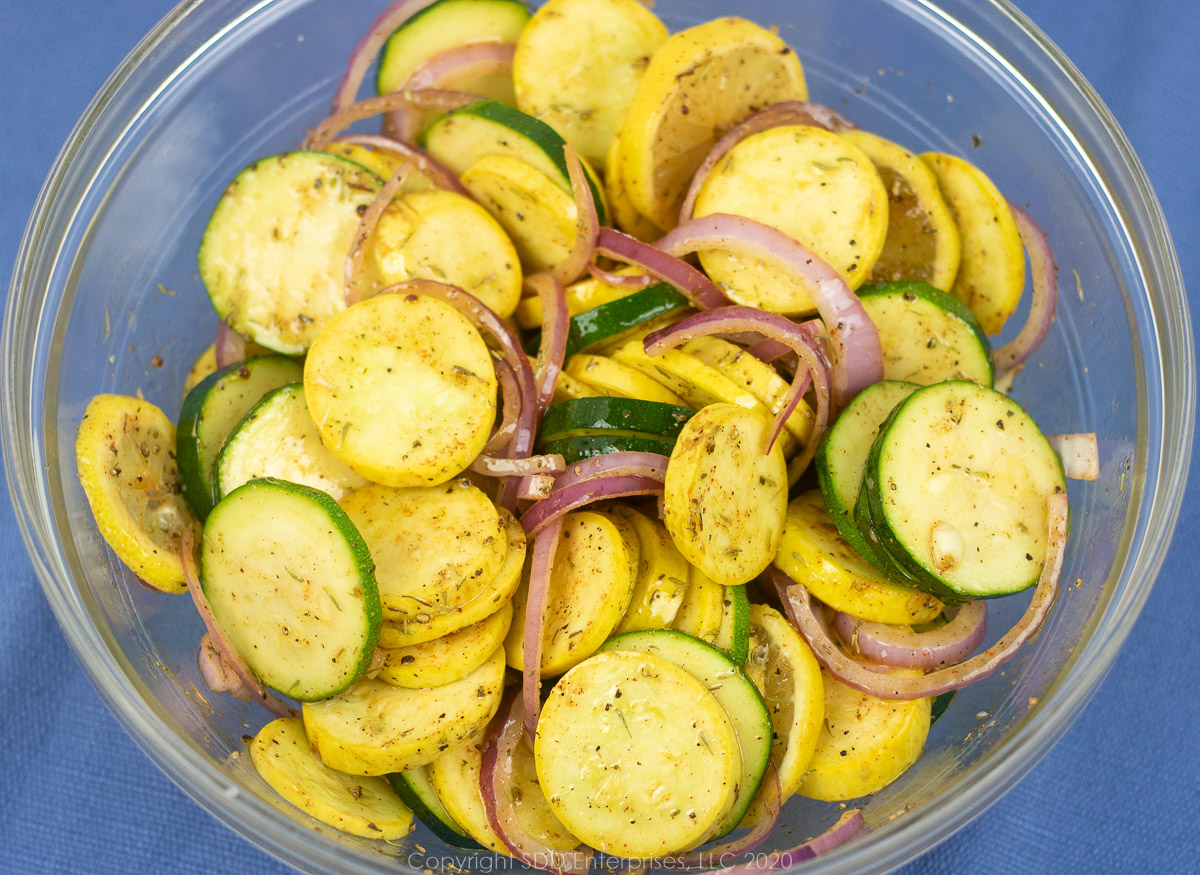 sliced squash and zucchini mixed with onions, garlic, lemon and spices with olive oil in a glass bowl