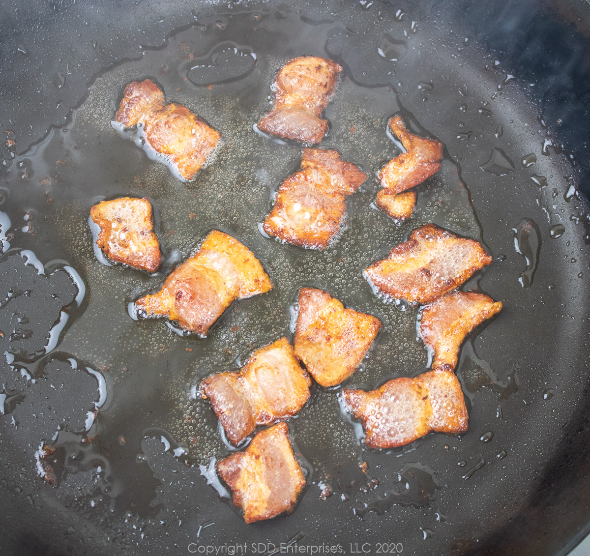 bacon pieces frying in a saute pan